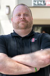 Ben Compton stands outside the Aztec Shops store arms crossed, wearing an SDSU polo shirt.